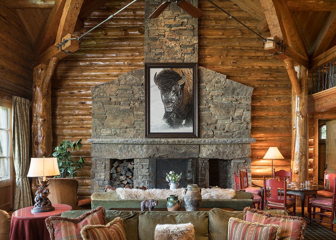 A rustic living area with log walls and a large stone fireplace featuring a bison portrait.