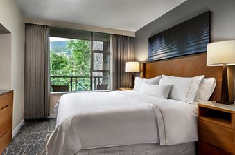 A spacious bedroom within The Westin Resort Two Bedroom Suite, featuring a large bed with white linens, two bedside lamps, and a floor-to-ceiling window overlooking a lush, green mountain landscape.