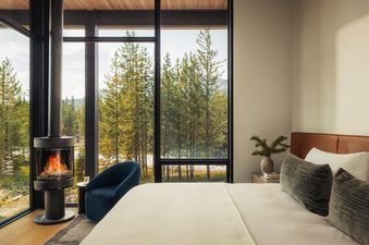A modern, bright bedroom in the Four Bedroom Private Home Moonlight Basin featuring a fireplace and a beautiful forest view.