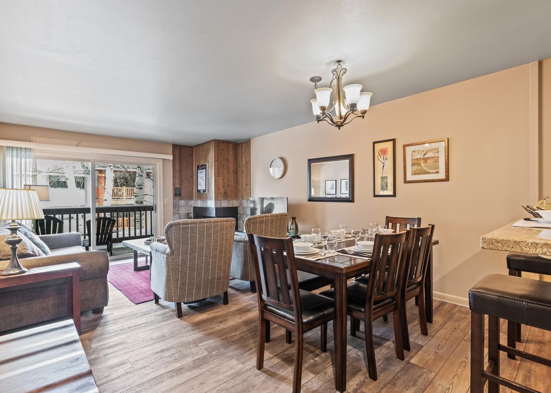 An inviting open-concept living and dining area at Snow Flower 107 Park City, featuring comfortable seating, a dining table set for a meal, a fireplace, and access to a balcony.