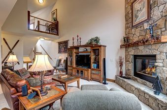 A living room with a large stone fireplace, a leather couch, a large television, and a large window with a view of a snow-capped mountain.