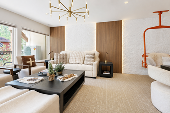 Contemporary alpine lounge area in Montaneros 302 with a plush white sofa, modern chandelier, and a unique decorative ski chair.