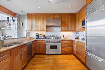 The kitchen of the Lumiere Two Bedroom Penthouse is fully equipped with stainless steel appliances, a double sink with a granite countertop, wood cabinets, and hardwood floors.