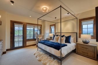 A master bedroom at Tanager Cabin 43 features a four-poster bed, wooden furnishings, and a glass door leading to a balcony with mountain views.