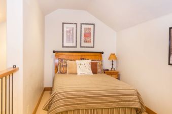 The bedroom in Terraces 602 features a comfortable double bed with a striped comforter, a side table with a lamp, and a wooden headboard.