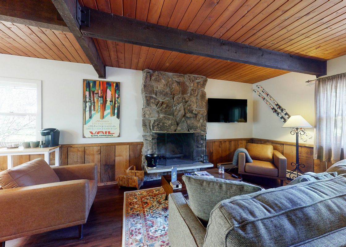 A cozy living room at Cozy Condo on Chamonix Lane with a stone fireplace, wood ceiling, comfortable seating, and ski-themed decor.
