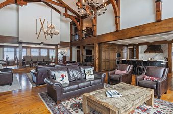 The spacious living area in Equinox at Empire Pass features exposed timber beams, leather furniture, and elegant lighting.