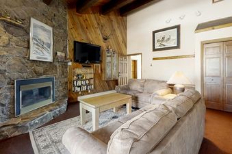 A cozy living room at Phoenix 216 features a stone fireplace, wood-paneled walls, and comfortable couches, creating a rustic yet inviting atmosphere.