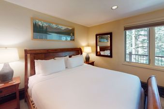 The bedroom in Manor Vail 187 features a king-size bed, two nightstands, a dresser, and a window with a view of the trees.