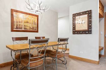 A cozy dining area at The Charter G2105 with a rustic wooden table, metal-framed chairs, an antler chandelier, and nature-themed artwork.