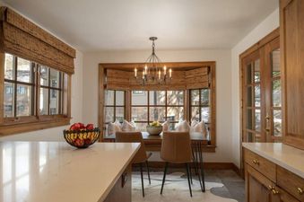 The dining area showcases a blend of modern and rustic elements, featuring comfortable seating, a stylish chandelier, and woven blinds that add texture to the space.