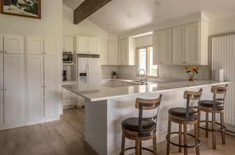 A modern kitchen with white cabinets, light countertops, and a large island with three bar stools.