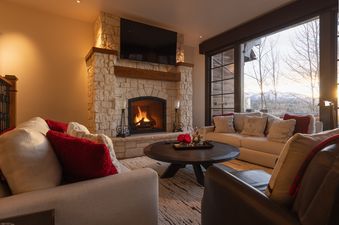 A cozy living room at the Ivory Stone Chalet at See Forever with a fireplace, comfortable sofas, and a scenic window view.