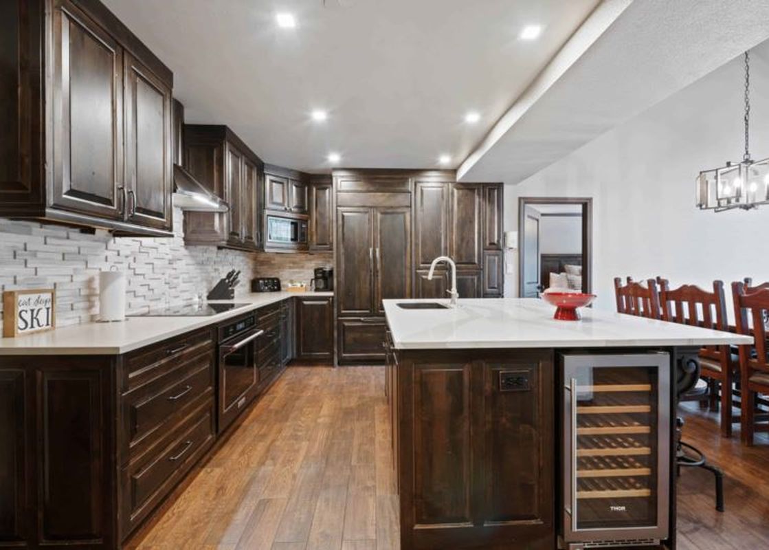 A modern kitchen at St James Place 437 features dark wood cabinetry, white countertops, a tiled backsplash, integrated appliances, a kitchen island with a wine cooler, and hardwood flooring.
