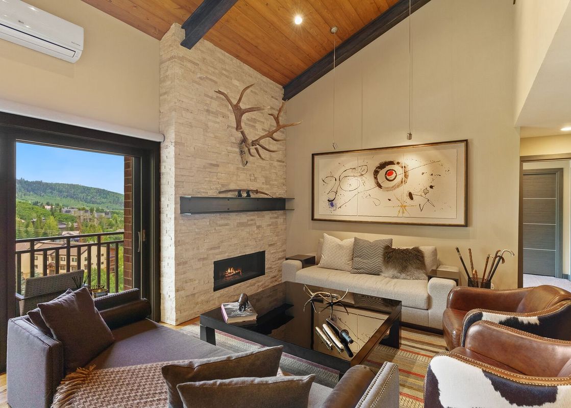 A cozy living room with a fireplace, a large window with a view of a mountain range, and two comfortable armchairs.