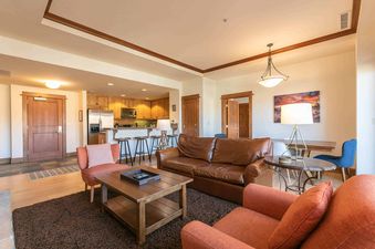 A living room in a condo with a leather sofa, two orange armchairs, and a wood coffee table.