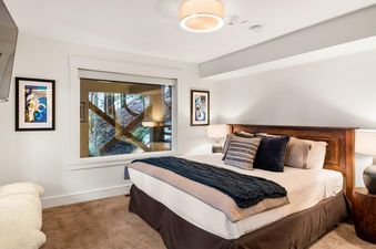 The bedroom in Northern Lights 42 features a cozy bed with decorative pillows and a view of the surrounding trees through a large window.