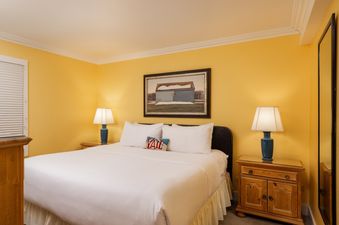 A cozy bedroom in Montaneros 311, featuring a king-sized bed with white linens, two wooden bedside tables with lamps, and a framed artwork above the bed.