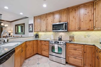 A well-lit kitchen featuring light-colored wooden cabinetry, granite countertops, and stainless steel appliances.