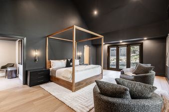A luxurious bedroom at Weedon Ranch features a four-poster bed, dark gray walls, and light wood flooring.