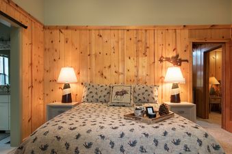 A cozy bedroom with a large bed, two lamps, and wooden paneled walls.
