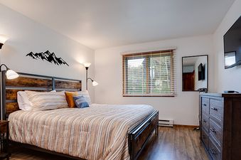 A cozy bedroom at Ranch at Steamboat RA101 featuring a king-sized bed, rustic wooden furniture, and a mountain-themed wall decal.