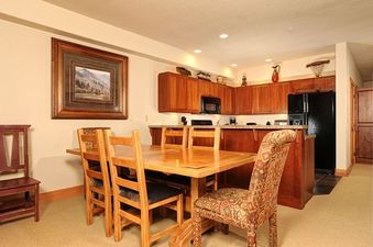 The kitchen and dining area in the Redhawk Townhome 3 Bedroom features a wooden dining table with four chairs and a spacious kitchen with wooden cabinetry and modern appliances.