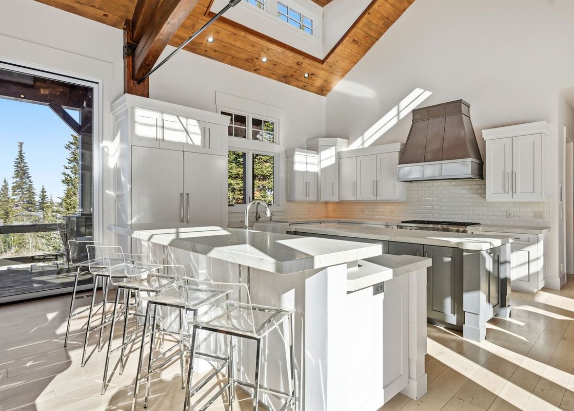 Modern kitchen with a marble island, white cabinetry, and wood-paneled vaulted ceilings.