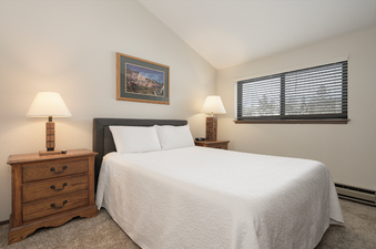 A cozy bedroom with a white bed, two wooden nightstands with lamps, and a window.
