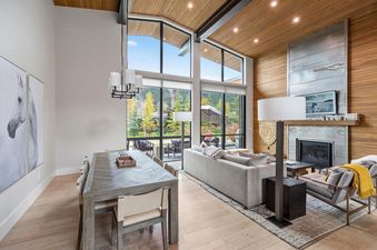 A modern, open-concept living and dining area with large windows, a fireplace, and stylish furnishings.