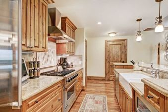 The kitchen at The Arrabelle One Bedroom features stainless steel appliances, granite countertops, and light wood cabinetry, with a cozy rug on the hardwood floor.
