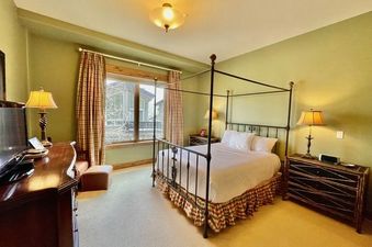 The primary bedroom at the Arrowhead Village Condominium Platinum 5 Bedroom features a comfortable canopy bed, an antique-style chest of drawers, and soft lighting for a relaxing retreat.