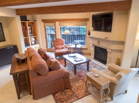 A cozy living room at The Chateaux Luxury One Bedroom, featuring comfortable seating, a fireplace, and a view of the outdoors through large windows.