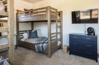 A cozy bunk room in Essentia Townhome 167A features a wooden bunk bed, a wall-mounted TV, and a dark blue dresser.