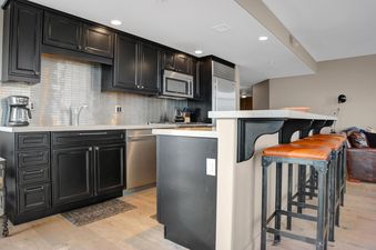 A modern kitchen in Lowell 301B with dark cabinetry, stainless steel appliances, and a breakfast bar with orange leather stools.