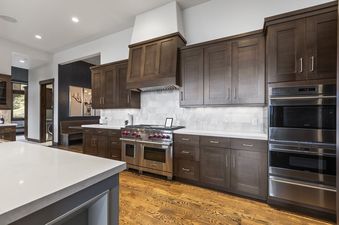 A modern kitchen in Ruby Run showcasing dark wood cabinetry, white countertops, a marble backsplash, and high-end stainless steel appliances including a Wolf range and double ovens.