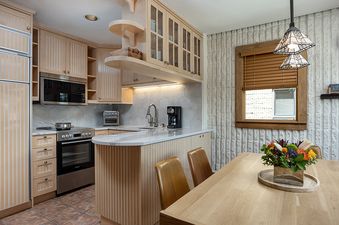 A bright and modern kitchen at Vail 21 406 with light wood cabinetry, stainless steel appliances, white countertops, and a dining area with a wooden table and chairs.