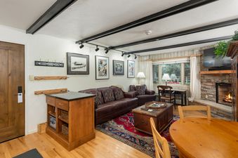 A cozy and inviting living area in Villa Valhalla 1 Bedroom Den Gold Unit 11, featuring a brown leather sofa, an armchair, a rustic coffee table, and a stone fireplace, creating a warm and comfortable ambiance.