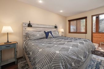 The bedroom at Kings Crossing Townhome 12 features a large bed with a patterned comforter, two nightstands with lamps, and a wooden headboard with wall-mounted lights.