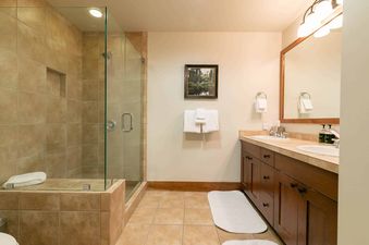 A bathroom with a large walk-in shower, double sinks, and a wooden vanity.