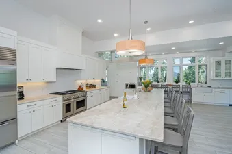 A spacious, modern kitchen at Turkey Creek, featuring white cabinetry, stainless steel appliances, a large marble-topped island with bar seating, and large windows offering views of trees and mountains.
