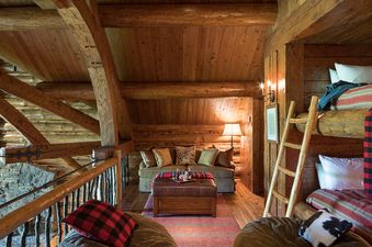 A cozy, rustic loft living area in The Grizzly Wulff Lodge with a sofa, leather ottoman, bunk beds, and exposed wooden beams.