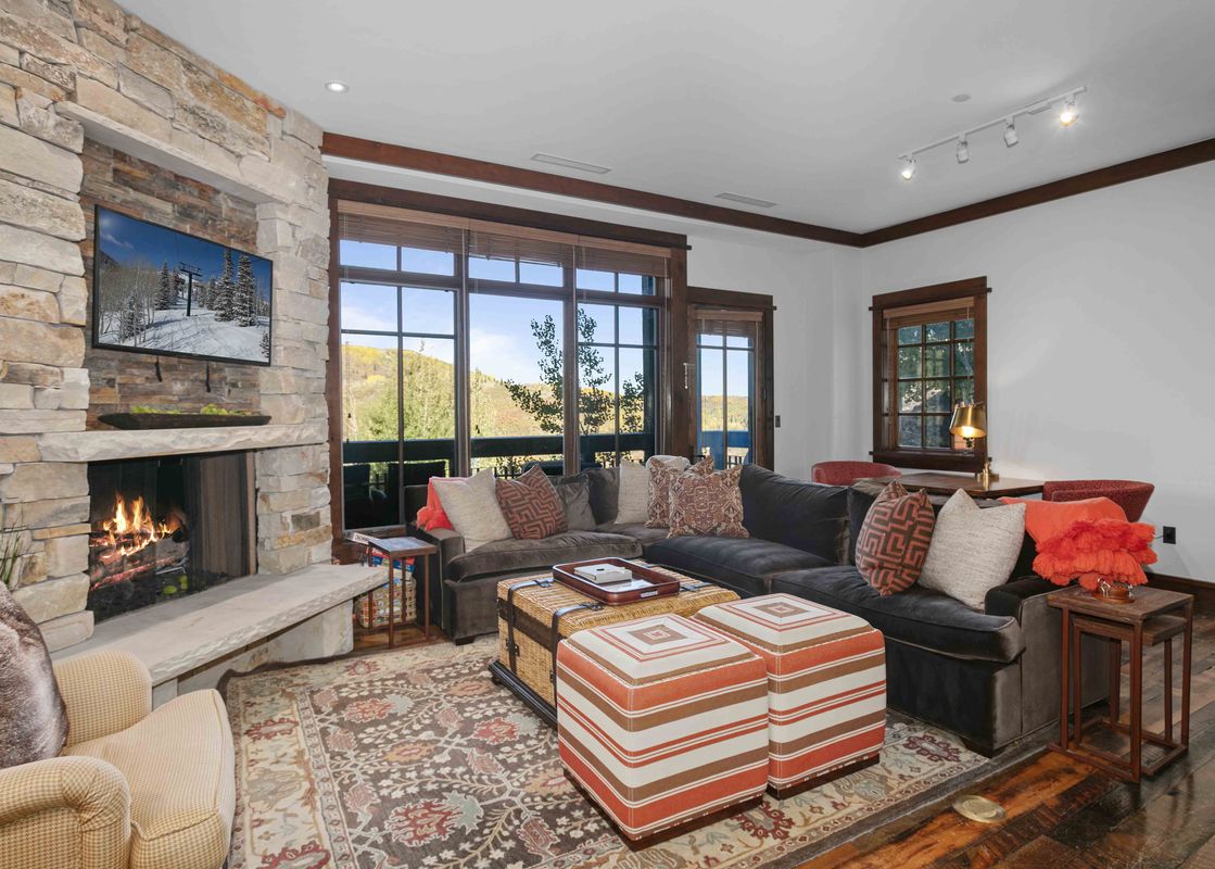 The Arrowleaf Lodge 205 living area features a stone fireplace, a large sectional sofa with colorful pillows, and expansive windows overlooking a mountain landscape.