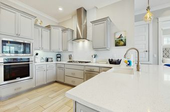 A modern kitchen in Prominence Moby Dick with light grey cabinets, stainless steel appliances, white subway tile backsplash, and light wood-look flooring.