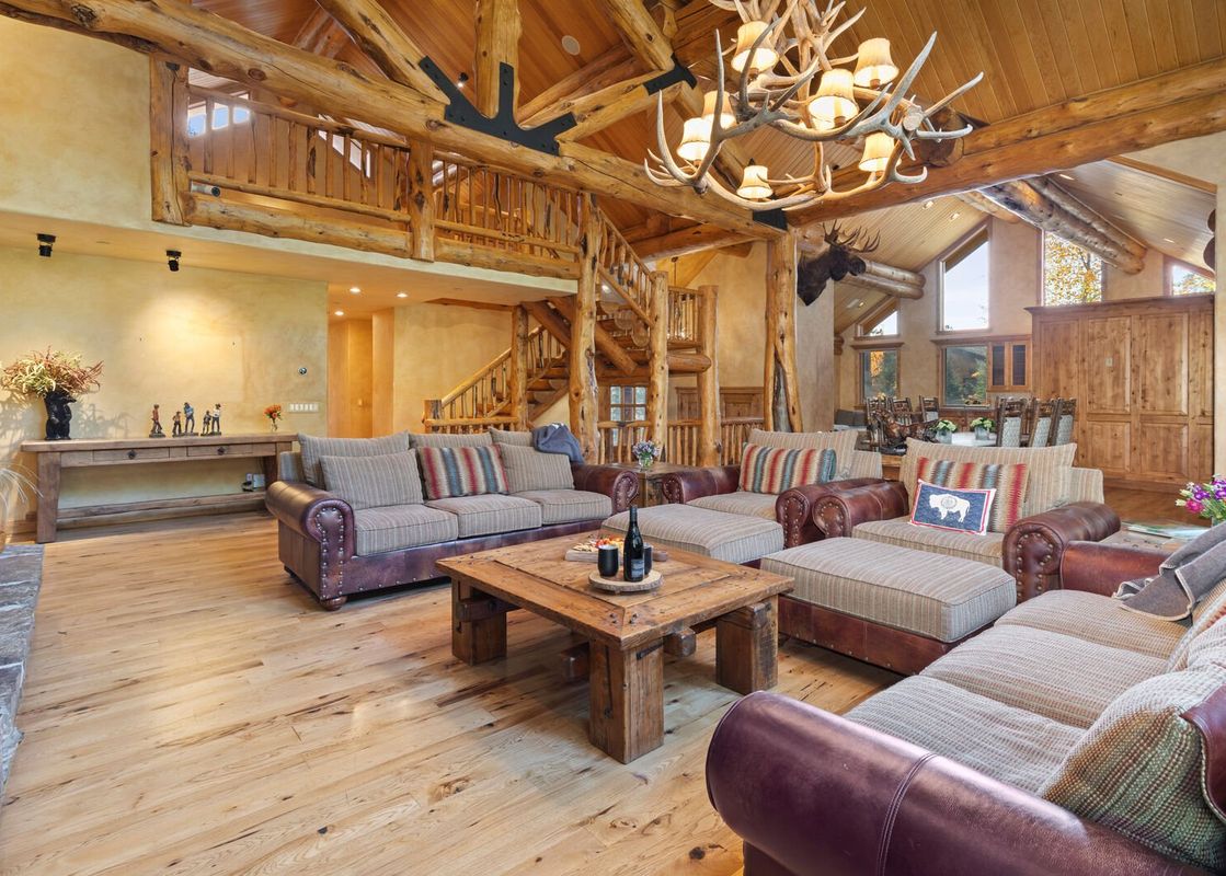 A spacious living room with a large sectional sofa, a coffee table, a fireplace, and a wooden staircase leading up to a loft.