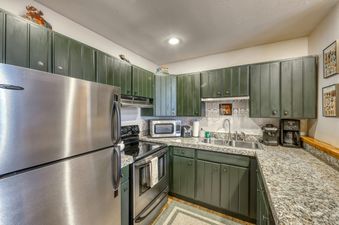 A kitchen with green cabinets, stainless steel appliances, and granite countertops.