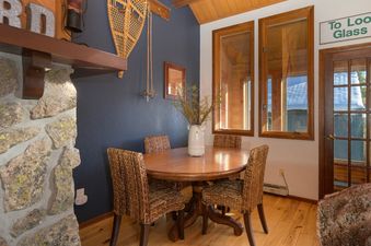 A rustic dining area with a round wooden table, four woven chairs, and charming decor including snowshoes on the wall and a stone fireplace.