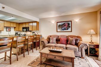 A cozy kitchen and living area with wood cabinets, granite countertops, a brown sofa, and a skiing artwork on the wall.