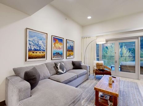 Living area at Bellas Mountain Vista with a grey sectional, a wooden coffee table, and glass doors leading to a balcony.