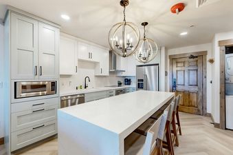 Westgate 4607AB kitchen features a white countertop island with bar stools, stainless steel appliances, and white cabinets.